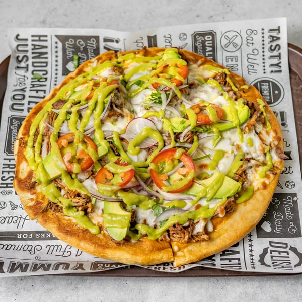 A pizza topped with meat, cheese, avocado, red onions, tomatoes, and a green sauce on a tray.