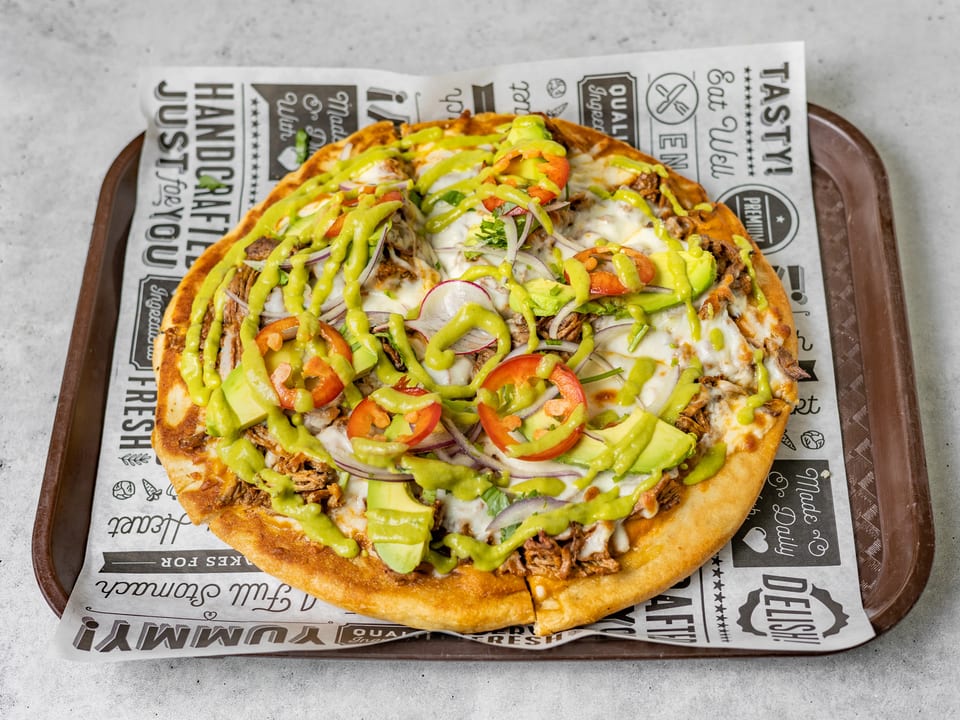 A pizza with pulled pork, avocado, red onion, tomatoes, and green sauce on branded paper.