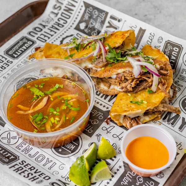 Birria tacos with melted cheese, cilantro, and red onions, served with consommé, lime, and sauce.
