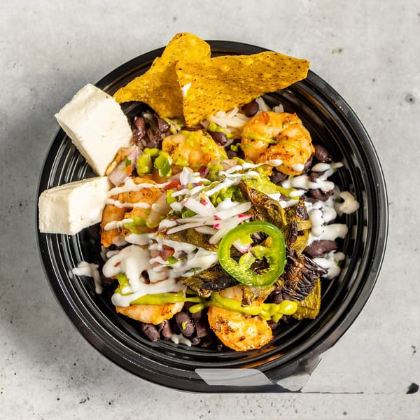A vibrant shrimp bowl with black beans, rice, cheese, tortilla chips, and various toppings.