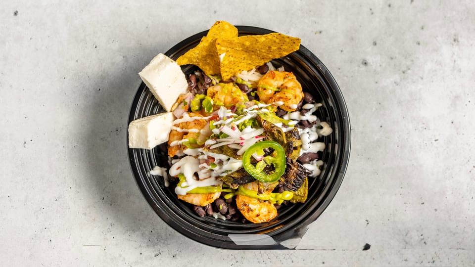 A vibrant shrimp bowl with black beans, rice, cheese, tortilla chips, and various toppings.