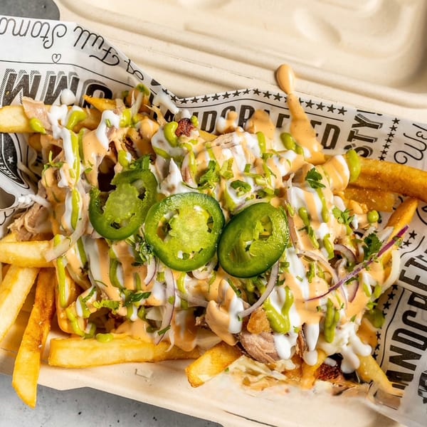 Loaded fries with sauces, jalapeños, and cilantro in a takeaway container with branded paper.