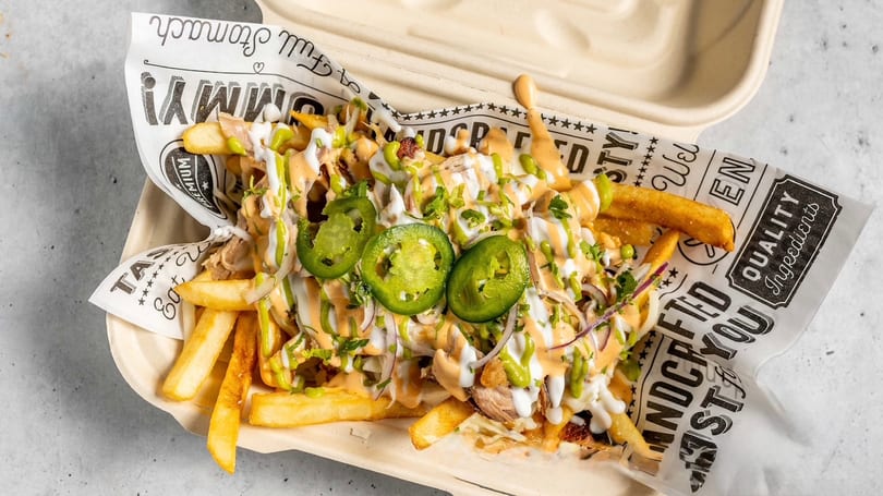 Loaded fries topped with sauces, jalapeños, and cilantro in a takeout container.