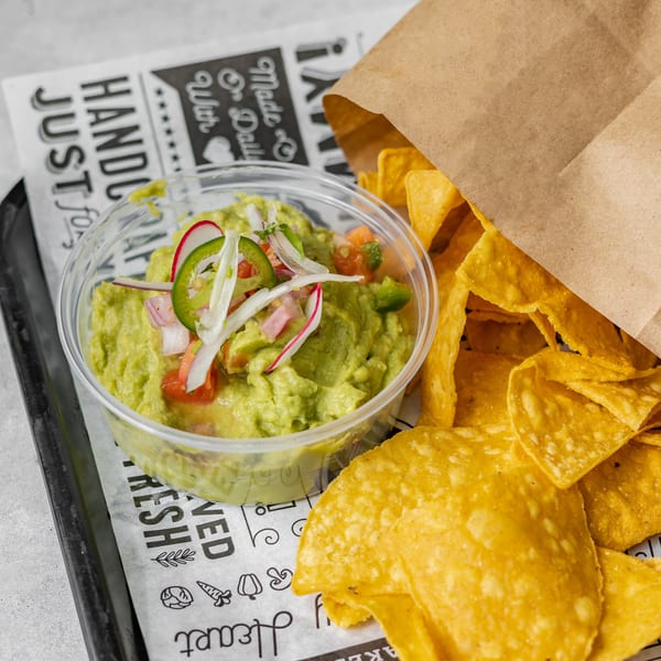 Guacamole with jalapeños, radishes, and onions, next to a bag of tortilla chips.