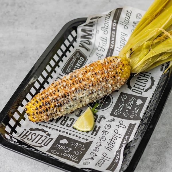 Grilled corn on the cob, topped with cheese and spices, served with a lime wedge.