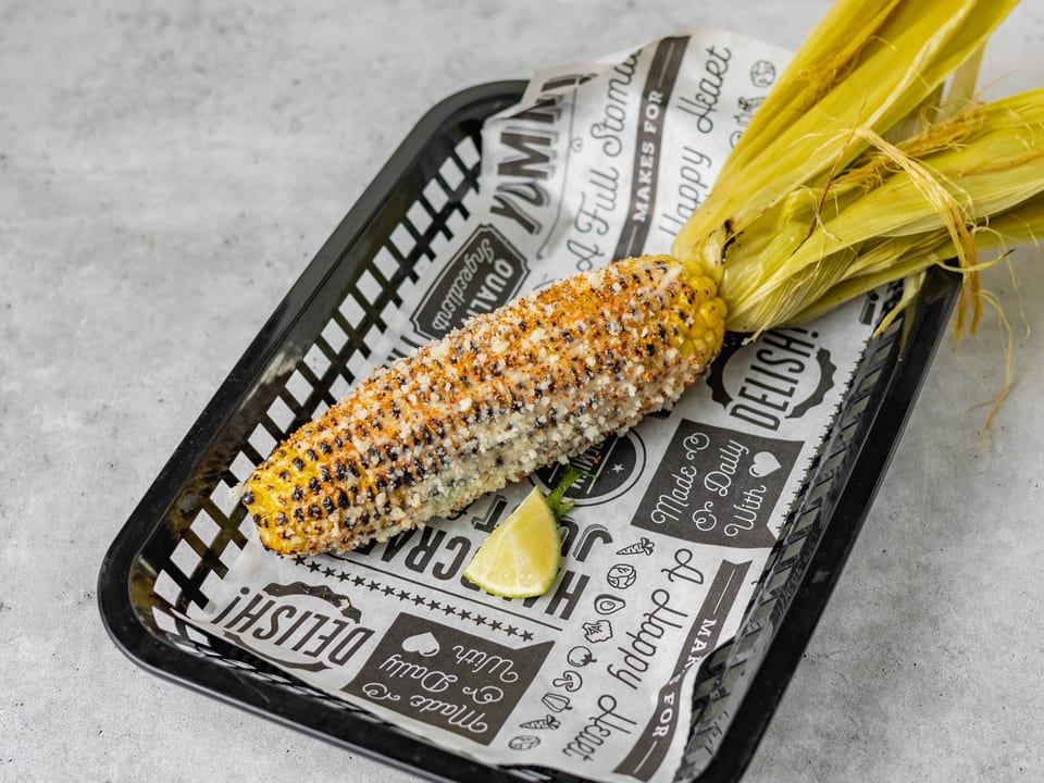 Grilled elote corn on the cob with cheese and chili powder, served with a lime wedge.