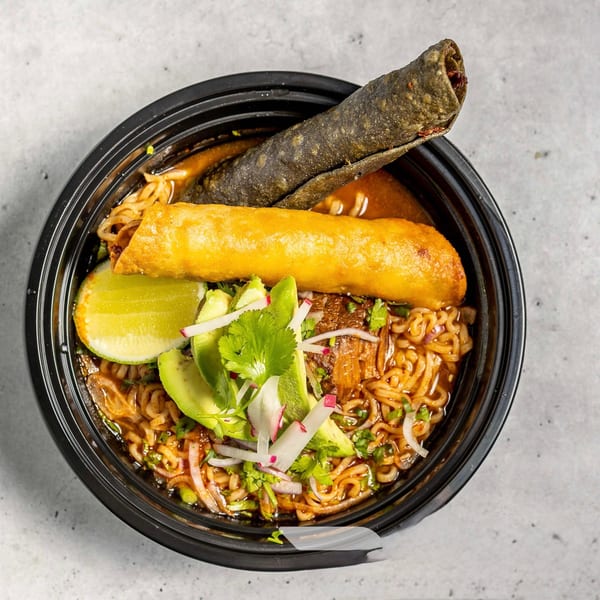 Ramen bowl with noodles, broth, avocado, lime, cilantro, radishes, and two taquitos.